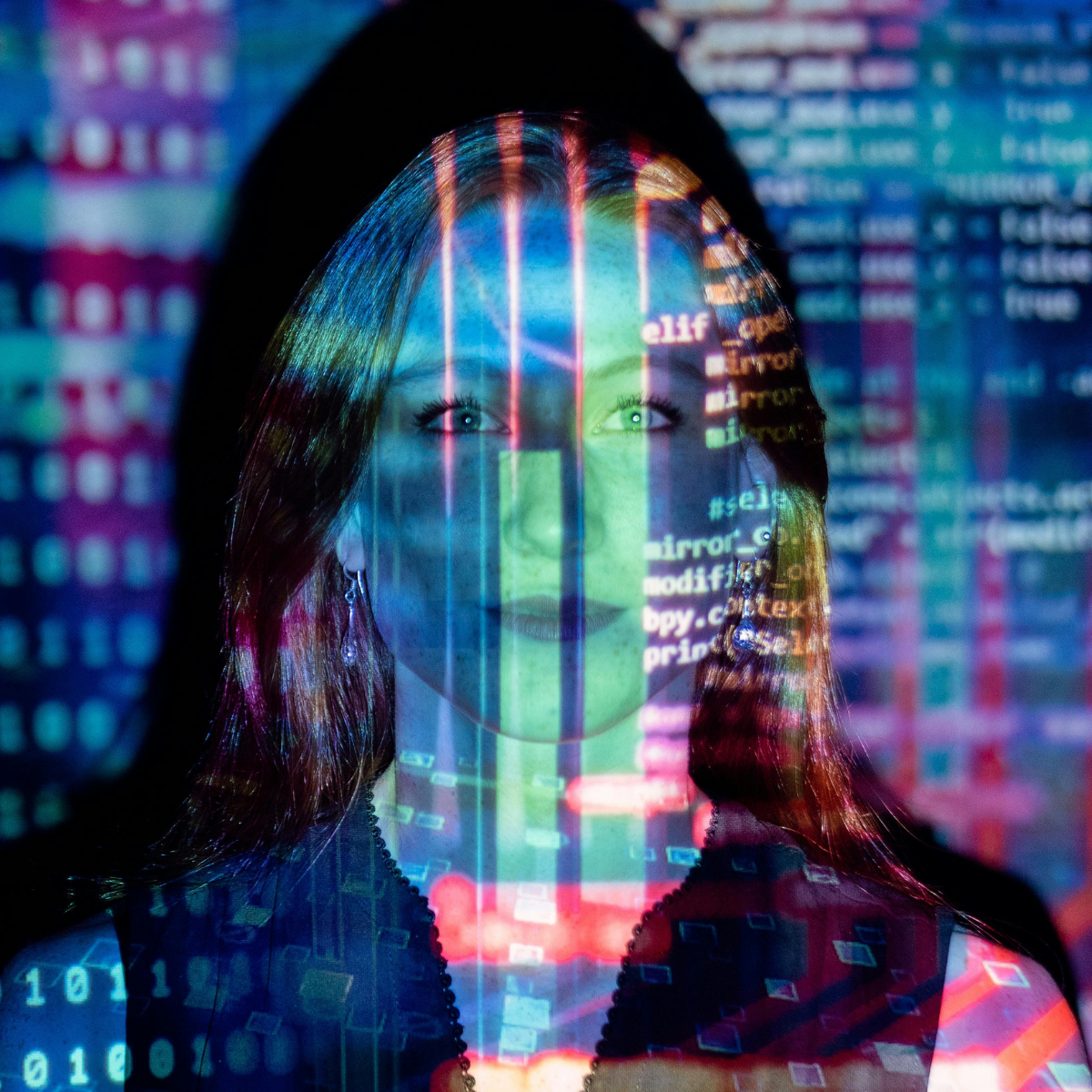 Woman stands in front of a wall of blue, red, purple, and white binary code, with the same binary code projected onto her face.