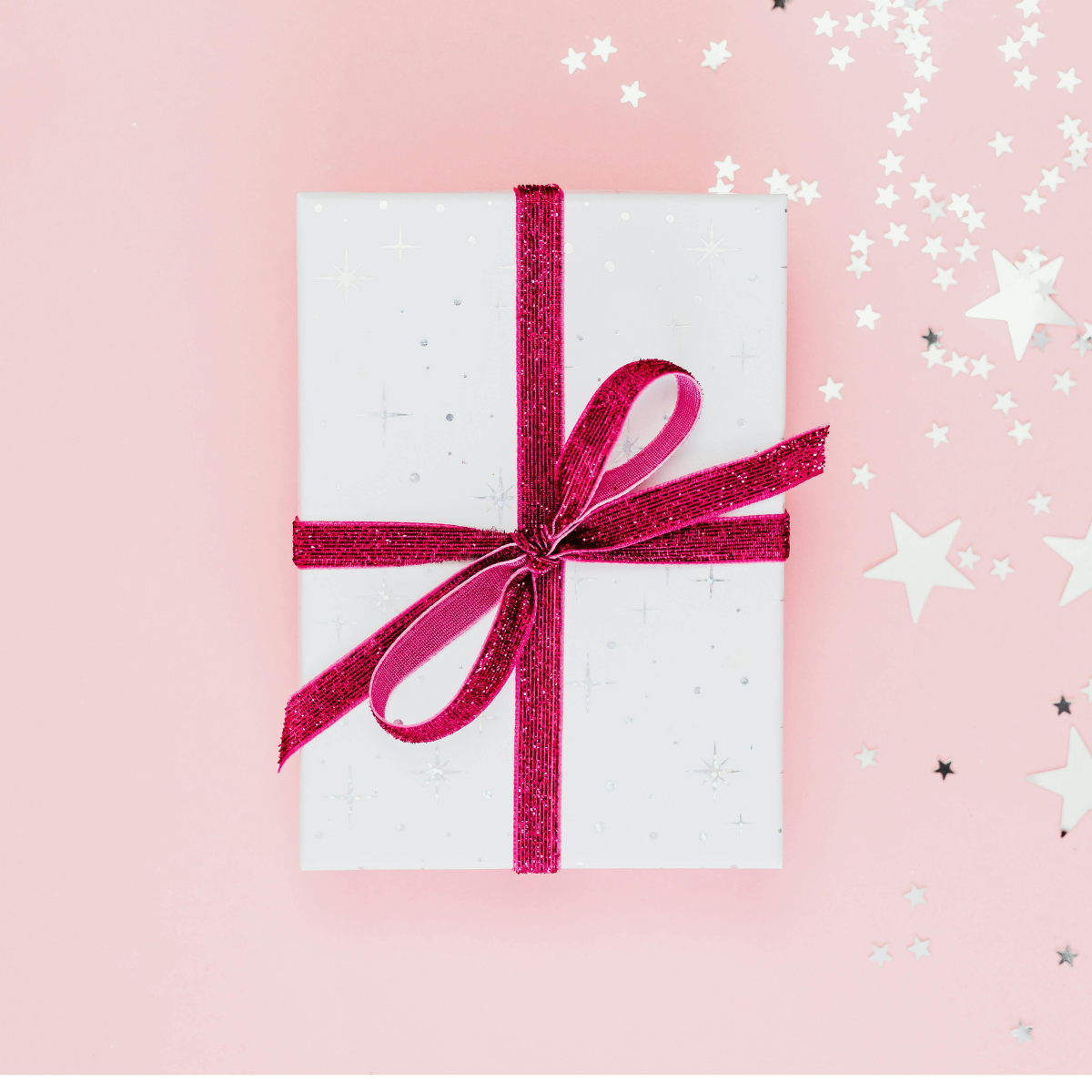 Pink background with gift wrapped in white with dark pink bow in the center. There are silver stars distributed on the right side of the image.