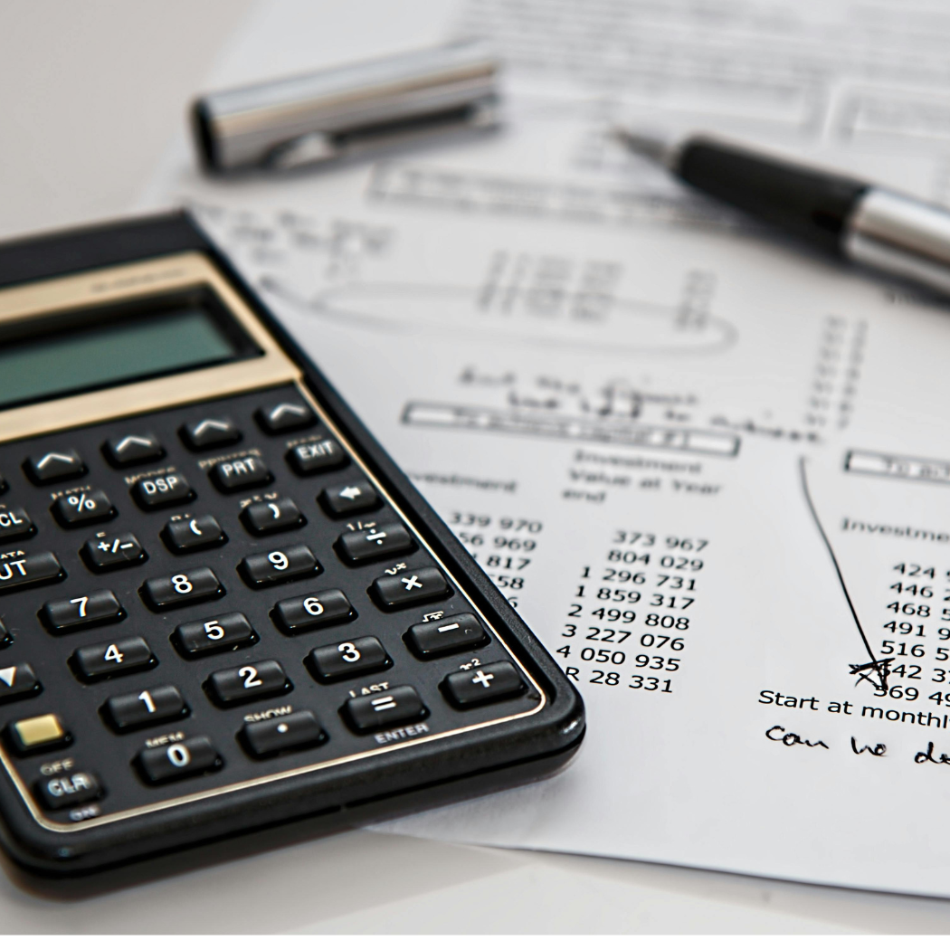 A black and gold calculator and ballpoint pen are laying on top of a piece of paper with numbers printed on it, like a budget.