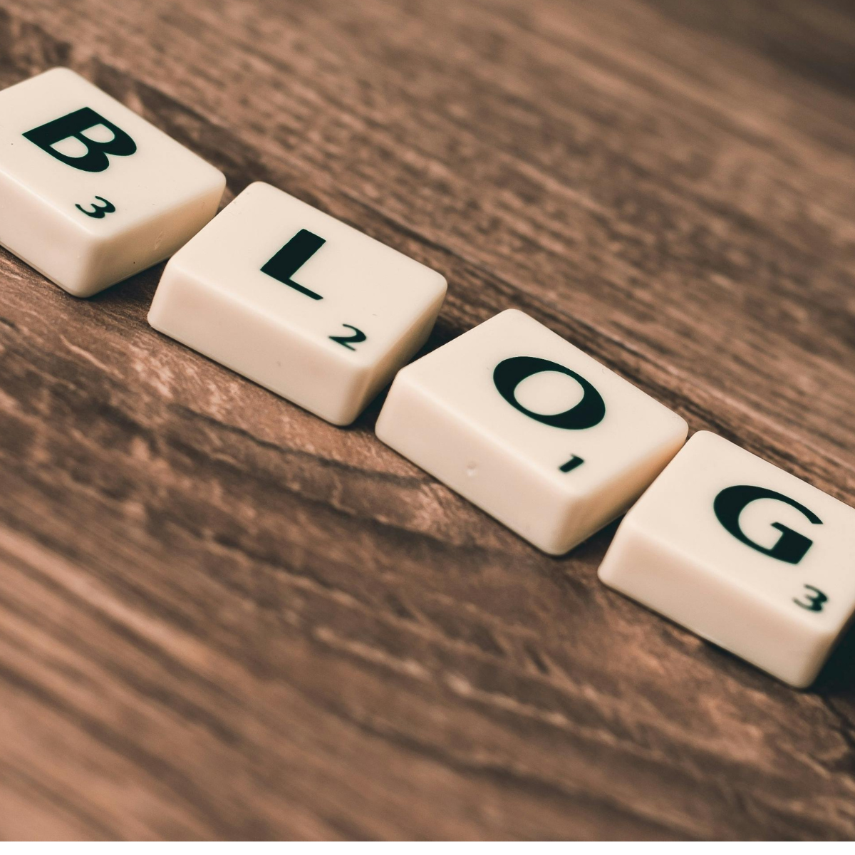 Scrabble letters appear close up on a brown wood background, spelling out the word "blog"