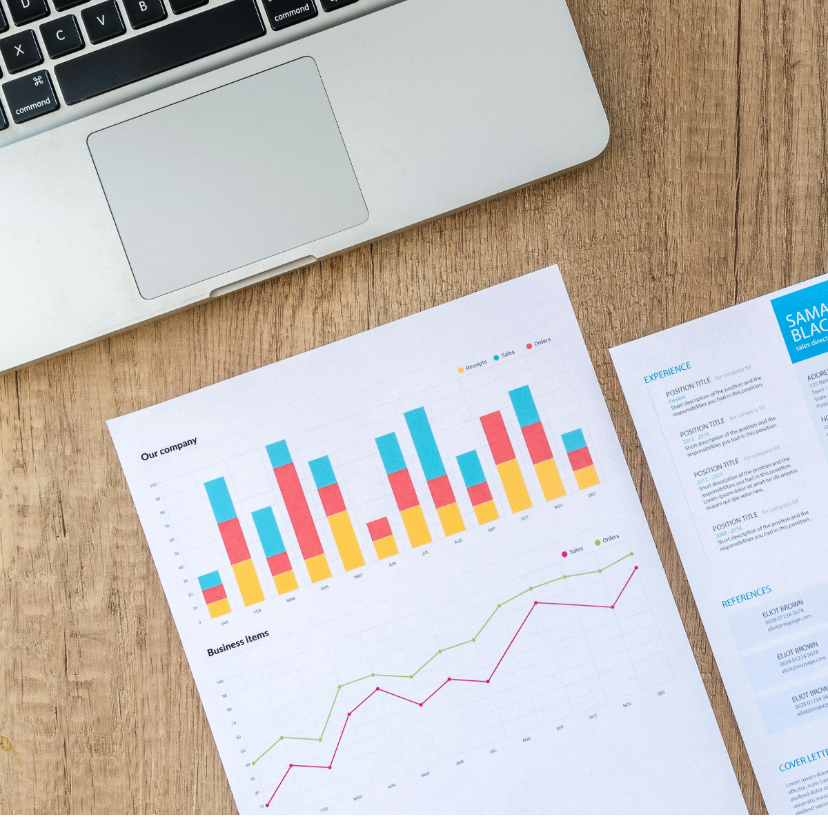 Marketing reports with graphs and a resume rest on a wooden table along with a laptop.