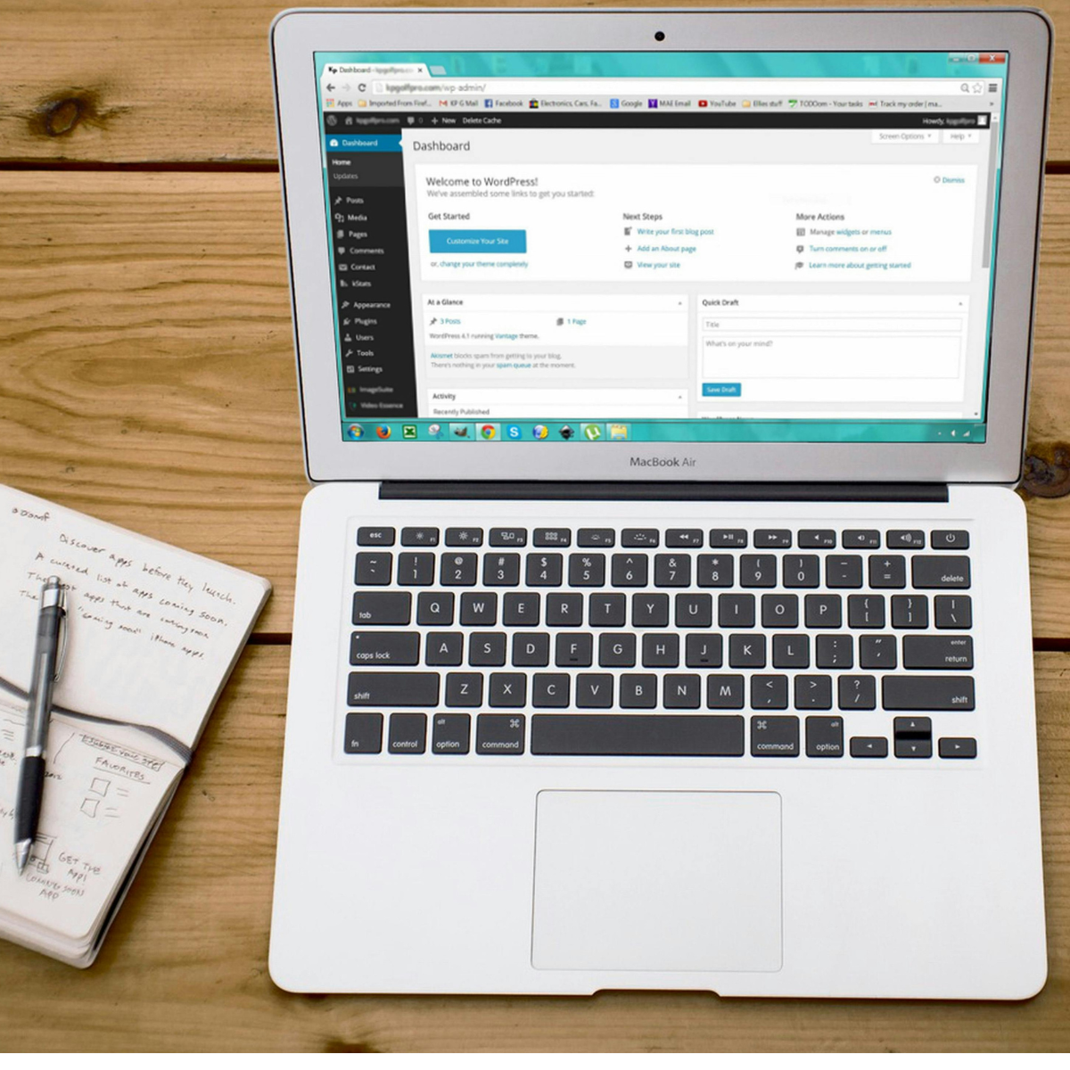 A notebook and pen sit next to an open laptop open to WordPress.