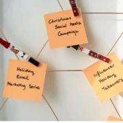 Three sticky notes are pinned to a white board with holiday themed clothespins and connected by string. One of the notes says Holiday Email Marketing Series.