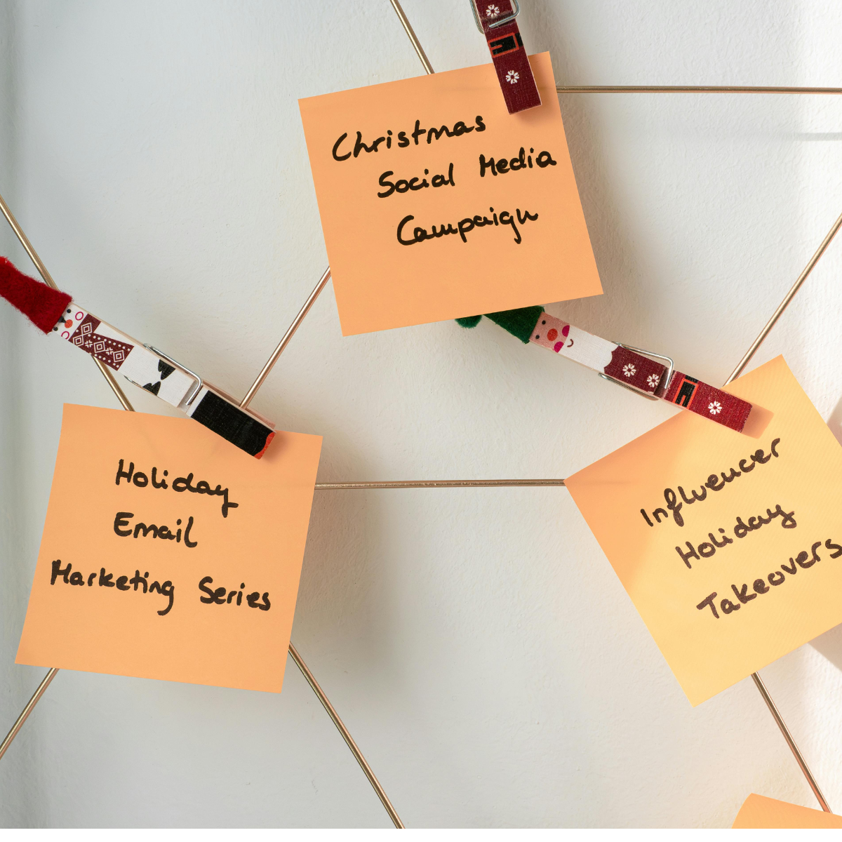 Three sticky notes are pinned to a white board with holiday themed clothespins and connected by string. One of the notes says Holiday Email Marketing Series.