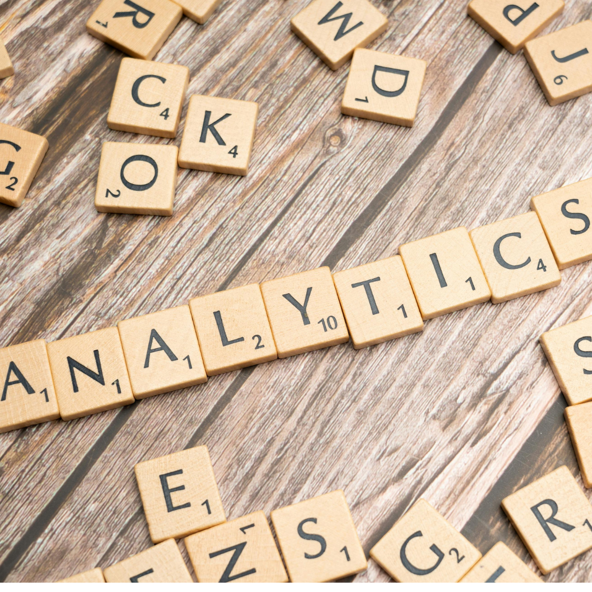 Scrabble letters are scattered on a wooden surface and the word "ANALYTICS" is centered.